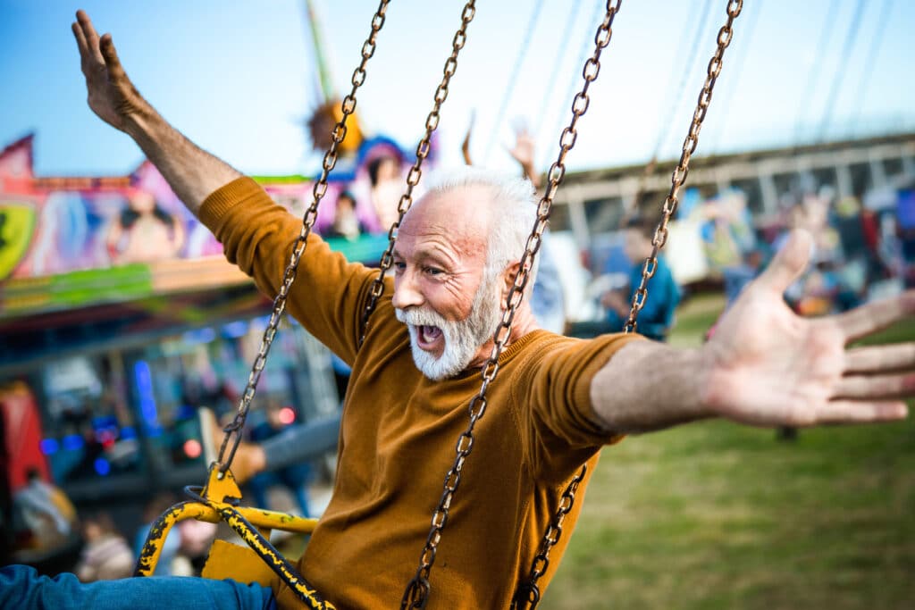 Happy senior man shouting while riding on chain swing with his arms outstretched at amusement park.