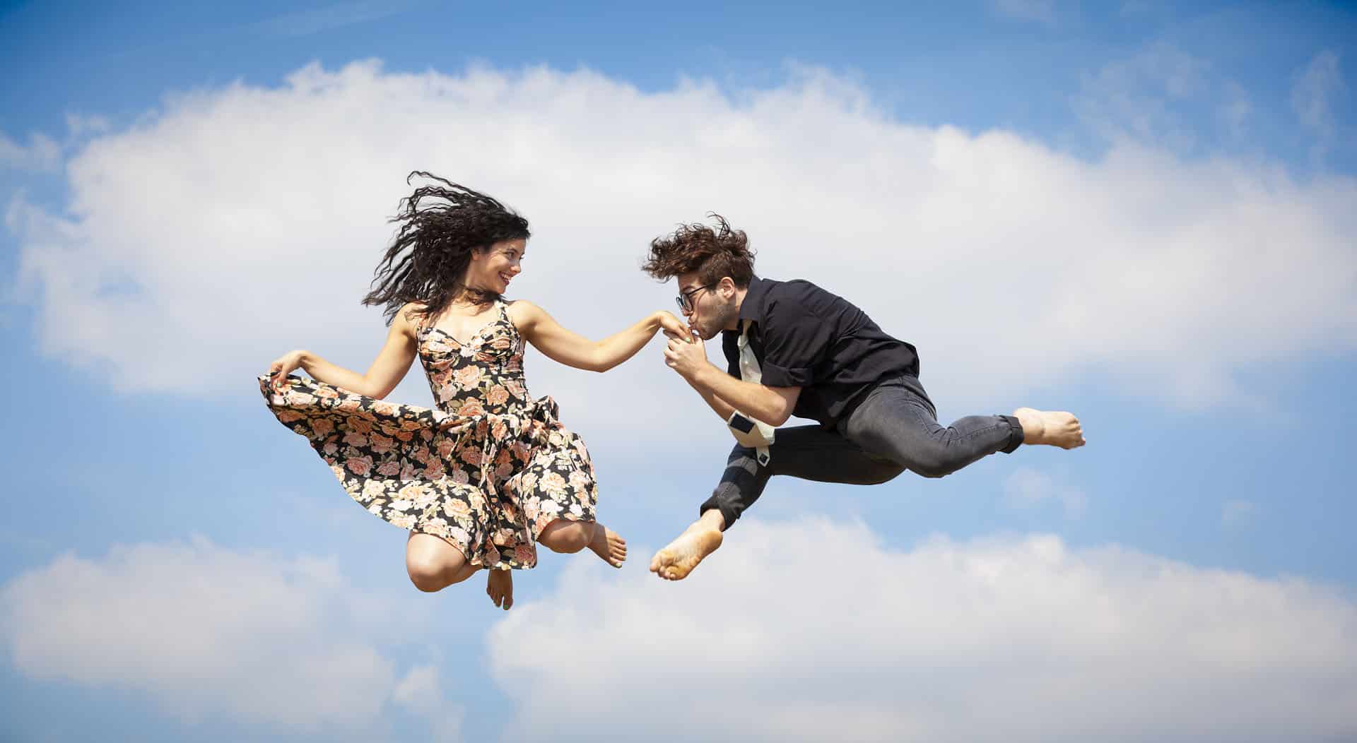 Happy jumping couple with hand kiss in mid-air.