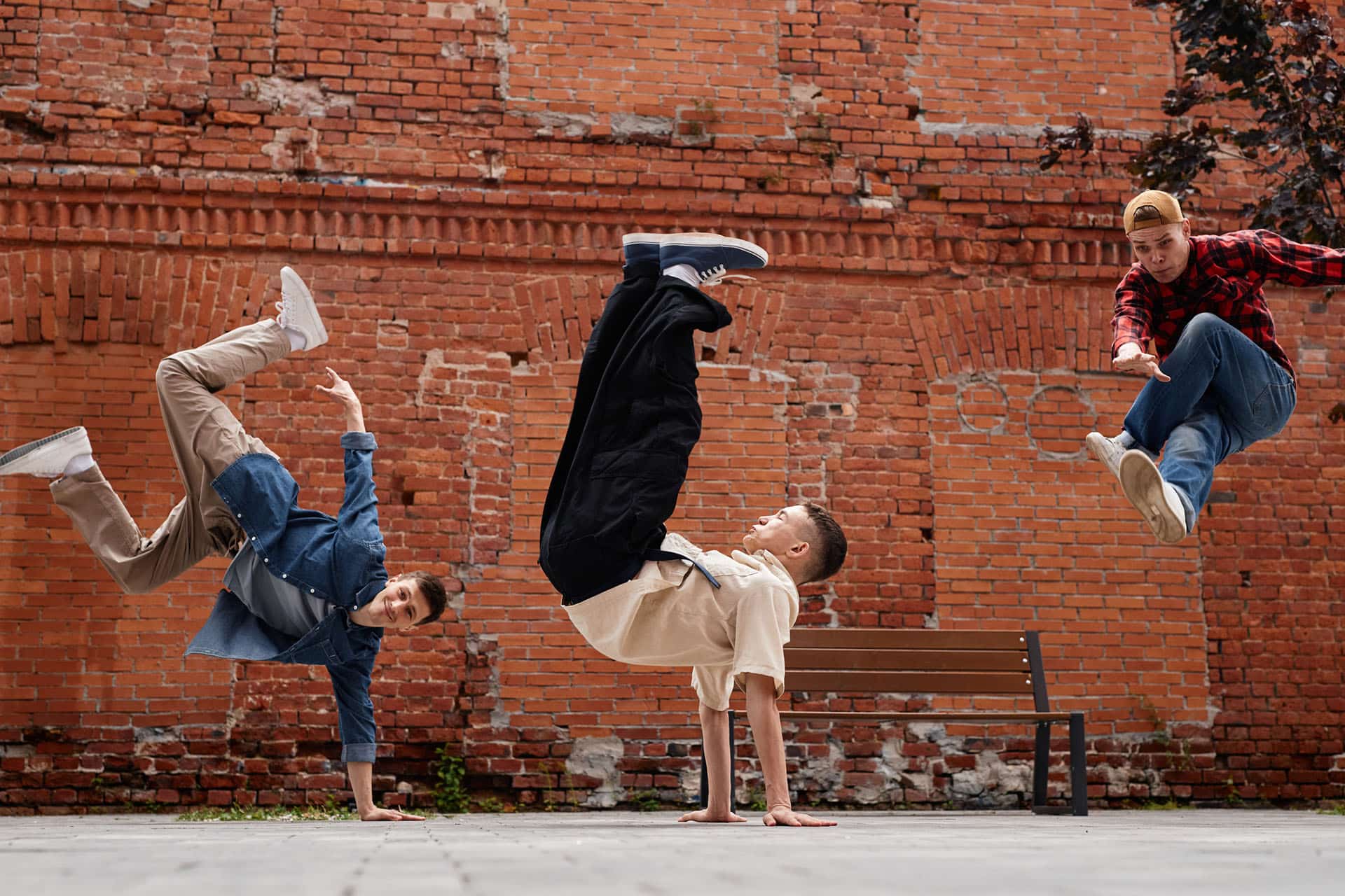 Freeze frame of all male breakdancing team jumping in air against brick wall outdoors