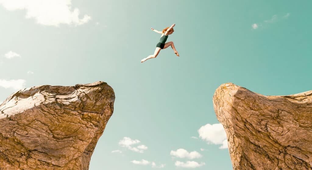 Concept of determination, adrenaline and over coming fear. Woman jumps from one rock formation to another. It is a dangerous jump and she uses all of her speed and strenght to make it across.
